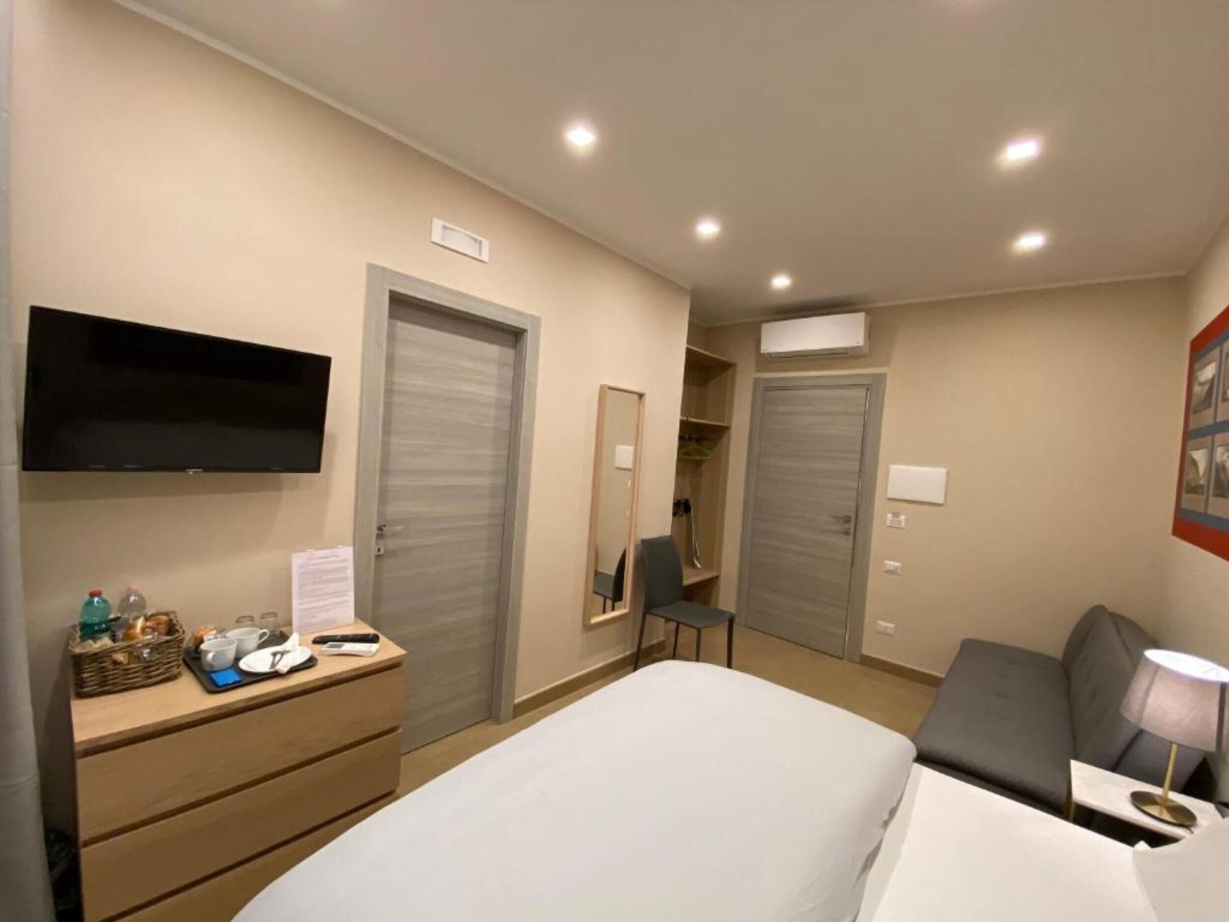 A hotel room with a bed, a desk with a chair, a flat-screen TV, a wardrobe, and a mirror.