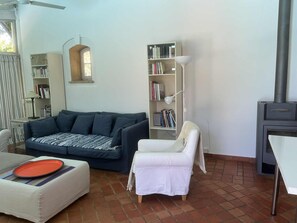 Ein Wohnzimmer mit einer Couch, einem weißen Sessel, einem Bücherregal, einer Lampe und einem Kamin.