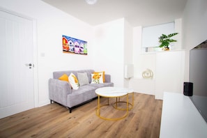Ein modernes Wohnzimmer mit einem grauen Sofa, einem kleinen runden Tisch und einem farbenfrohen Gemälde an der Wand.