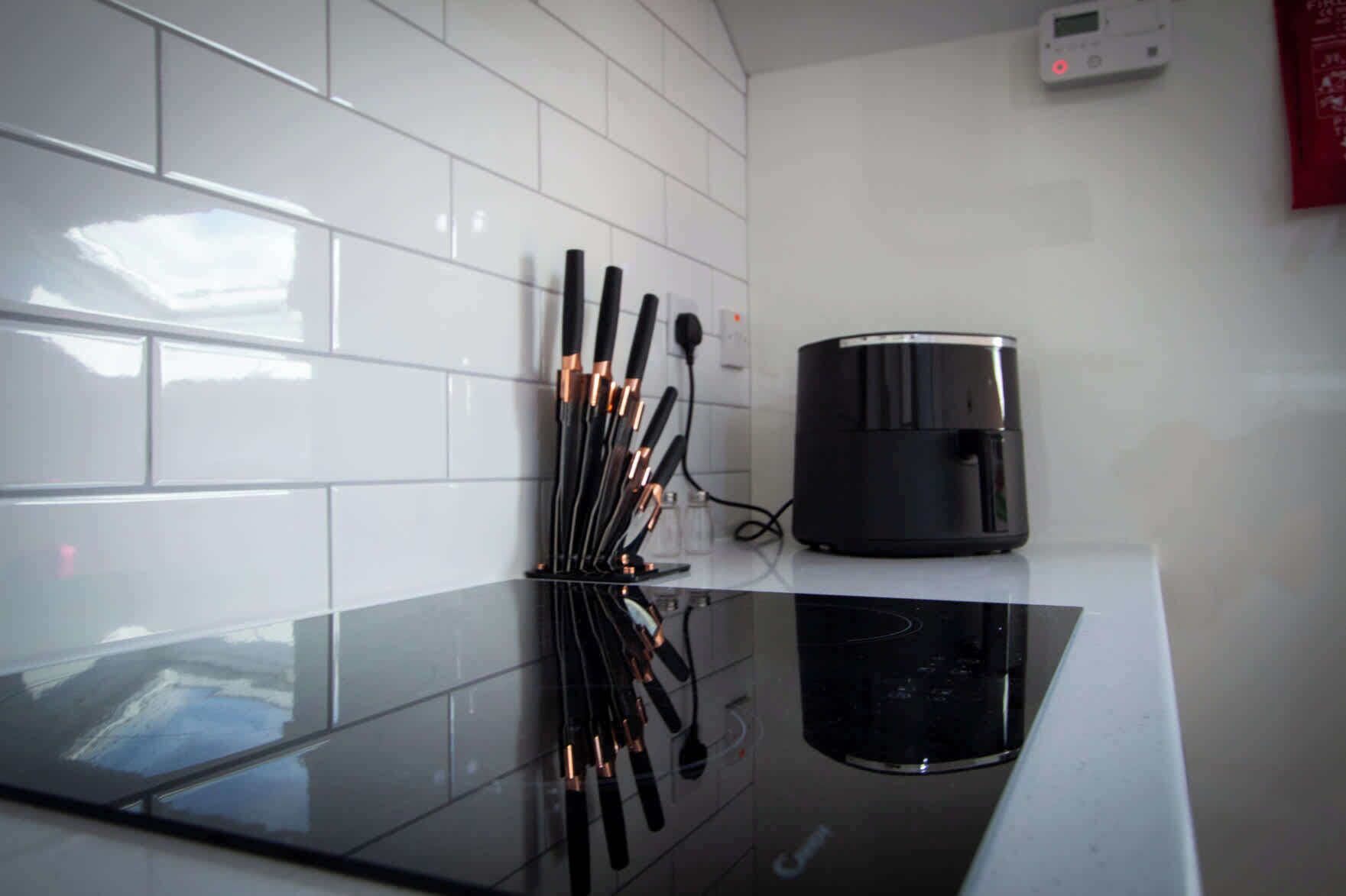 A kitchen with white tiled walls, a black countertop, and a coffee maker.