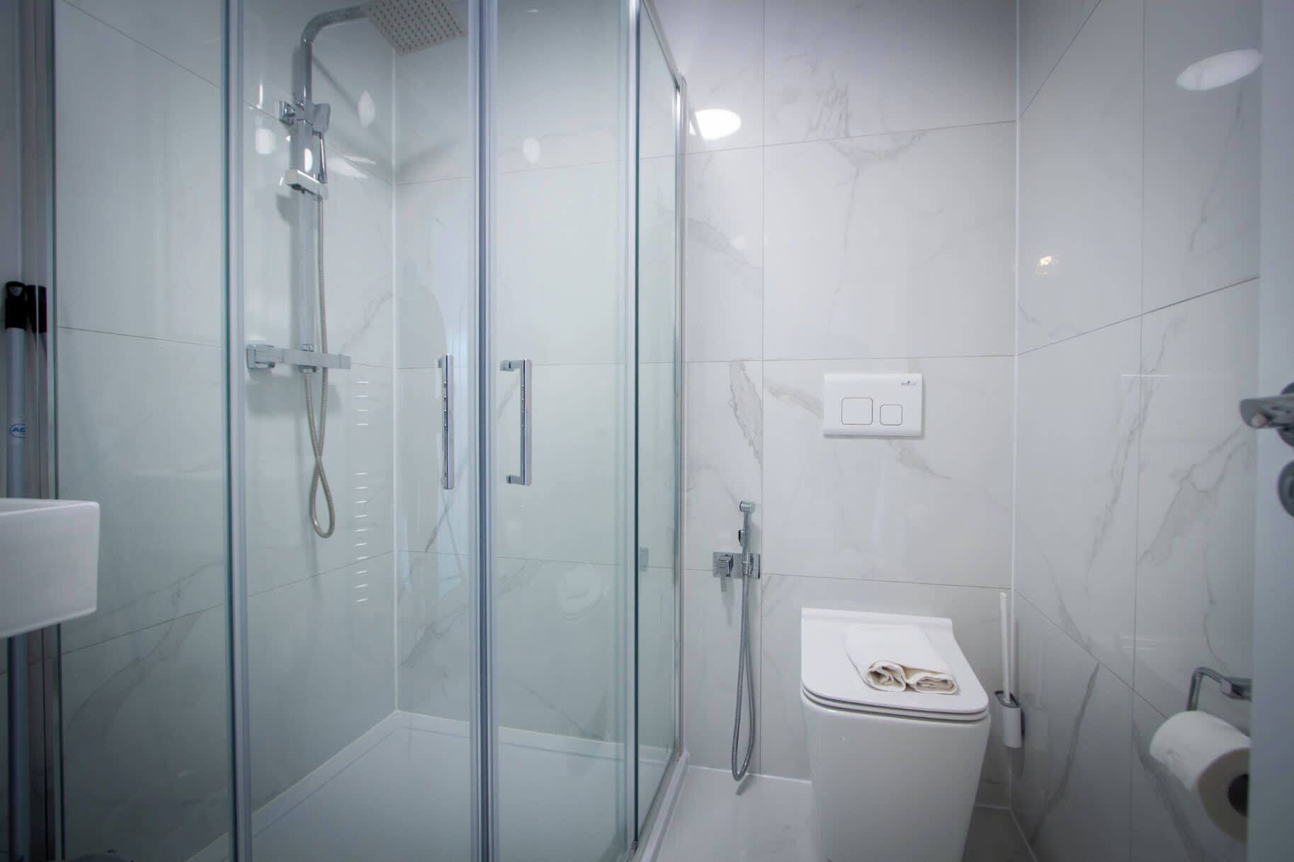 A modern bathroom with a glass-enclosed shower, a white sink, and a toilet.