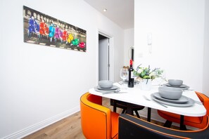 Ein Essbereich mit einem weißen Tisch, orangefarbenen Stühlen und einem farbenfrohen Wandbild.