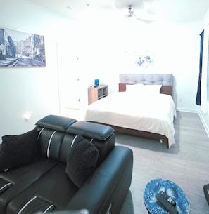 Una habitación de hotel moderna con cama, sofá, una mesita y un cuadro en la pared.