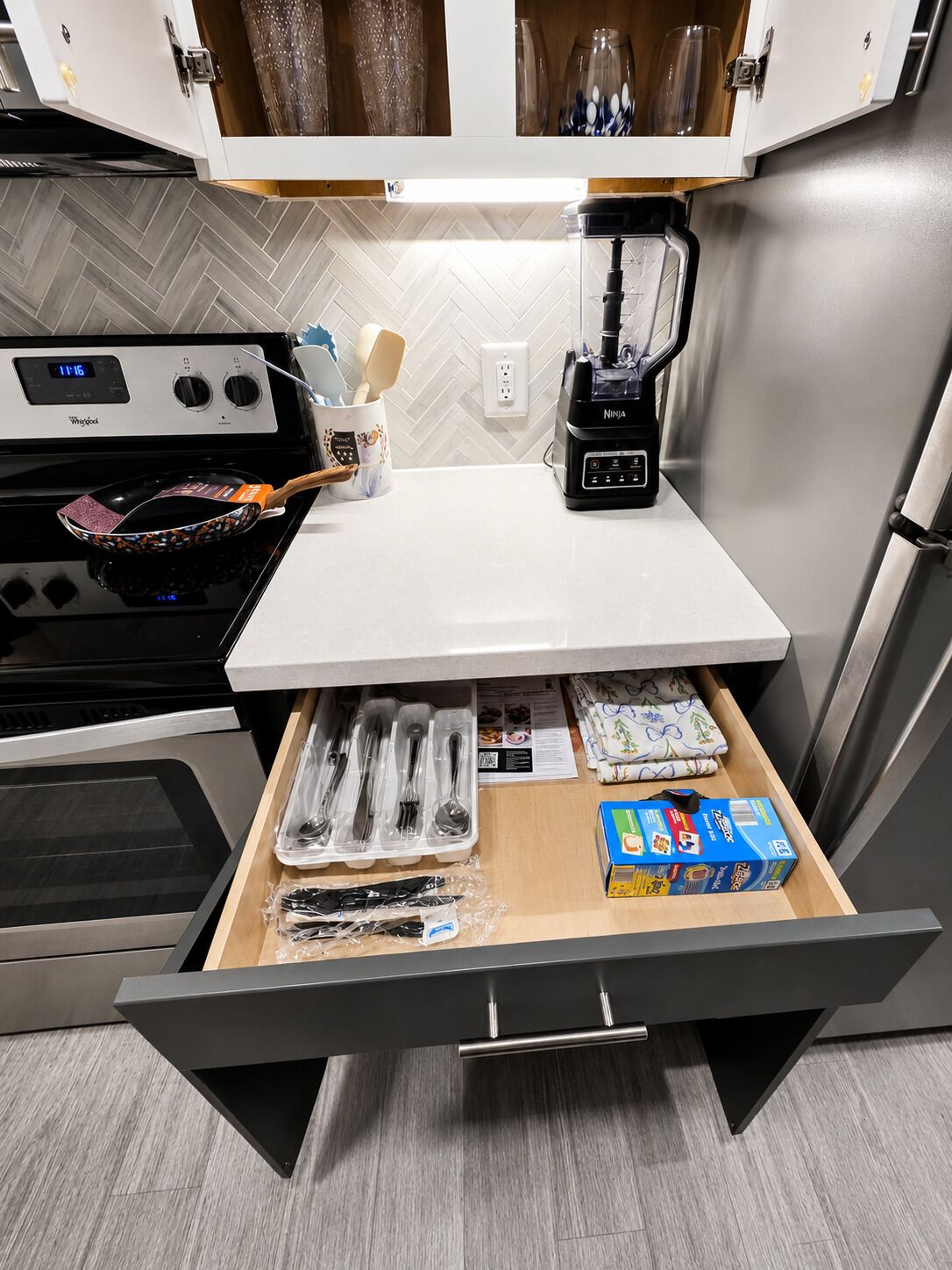 Una cocina equipada con microondas, licuadora, estufa y un cajón con utensilios.