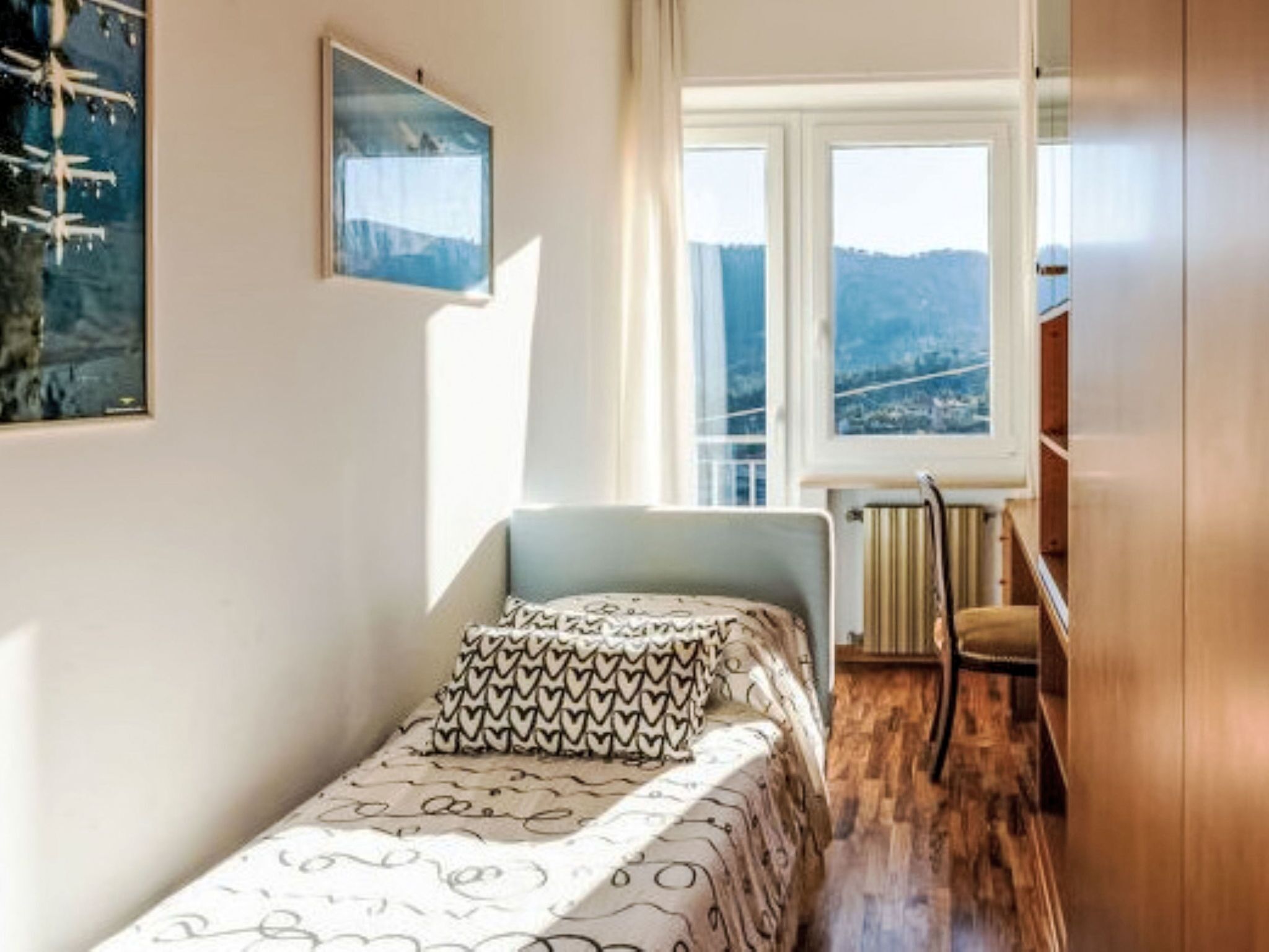 Ein kleines Schlafzimmer mit einem Bett, einem Heizkörper, einem Fenster mit Blick und einem Sessel.
