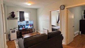 A compact living space with a sofa, a television, a radiator, and a clock on the wall.