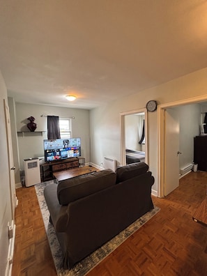 Ein kleiner Wohnraum mit einer Couch, einem Fernseher, einer Heizung und einer Uhr an der Wand.