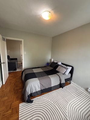 Ein Schlafzimmer mit einem Bett, einem Nachttisch, einem Sessel und einer Tür zu einem anderen Raum.