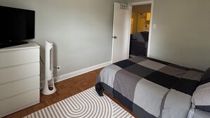 A bedroom with a bed, a TV, a fan, and a door leading to another room.