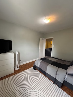 Ein Schlafzimmer mit einem Bett, einem Fernseher, einem Ventilator und einer Tür zu einem anderen Raum.