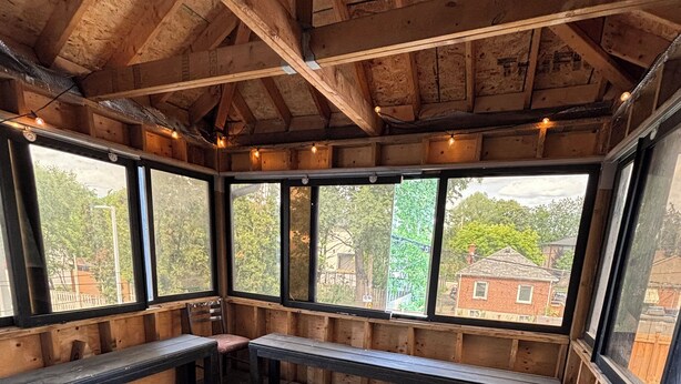A covered wooden deck with benches and large windows.