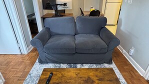 A living room with a gray sofa, a wooden coffee table, a TV, and a kitchen in the background.