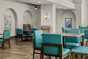 Un restaurante con sillas y mesas color turquesa, suelo de madera y secciones de techo abovedado.