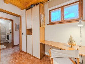 Ein Zimmer mit Holzboden, einem Schreibtisch mit Lampe, einem Stuhl, einem Fenster mit Jalousien und einem Kleiderschrank.
