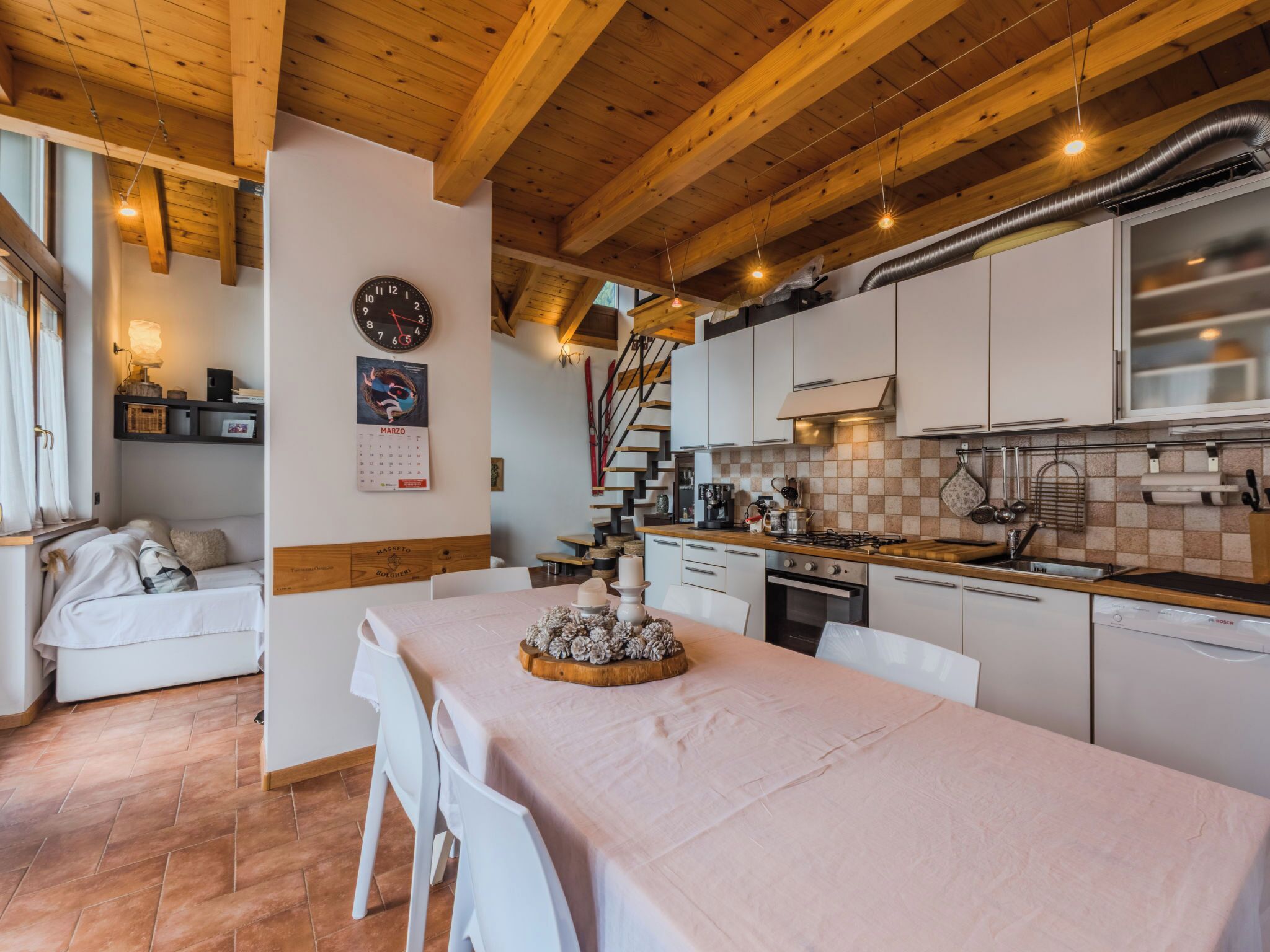 Una cocina acogedora con vigas de madera, un comedor con una mesa dispuesta para dos personas y un calendario en la pared.
