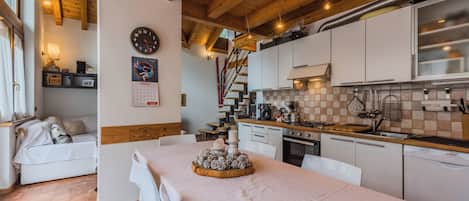 A cozy kitchen with wooden beams, a dining area with a table set for two, and a calendar on the wall.
