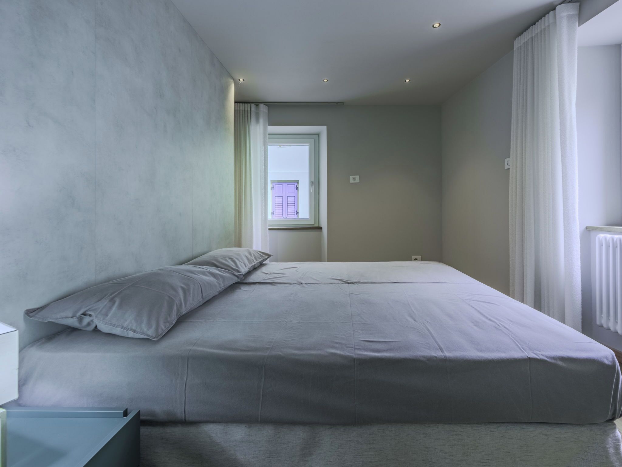 A bedroom with a bed, a window, and a radiator.