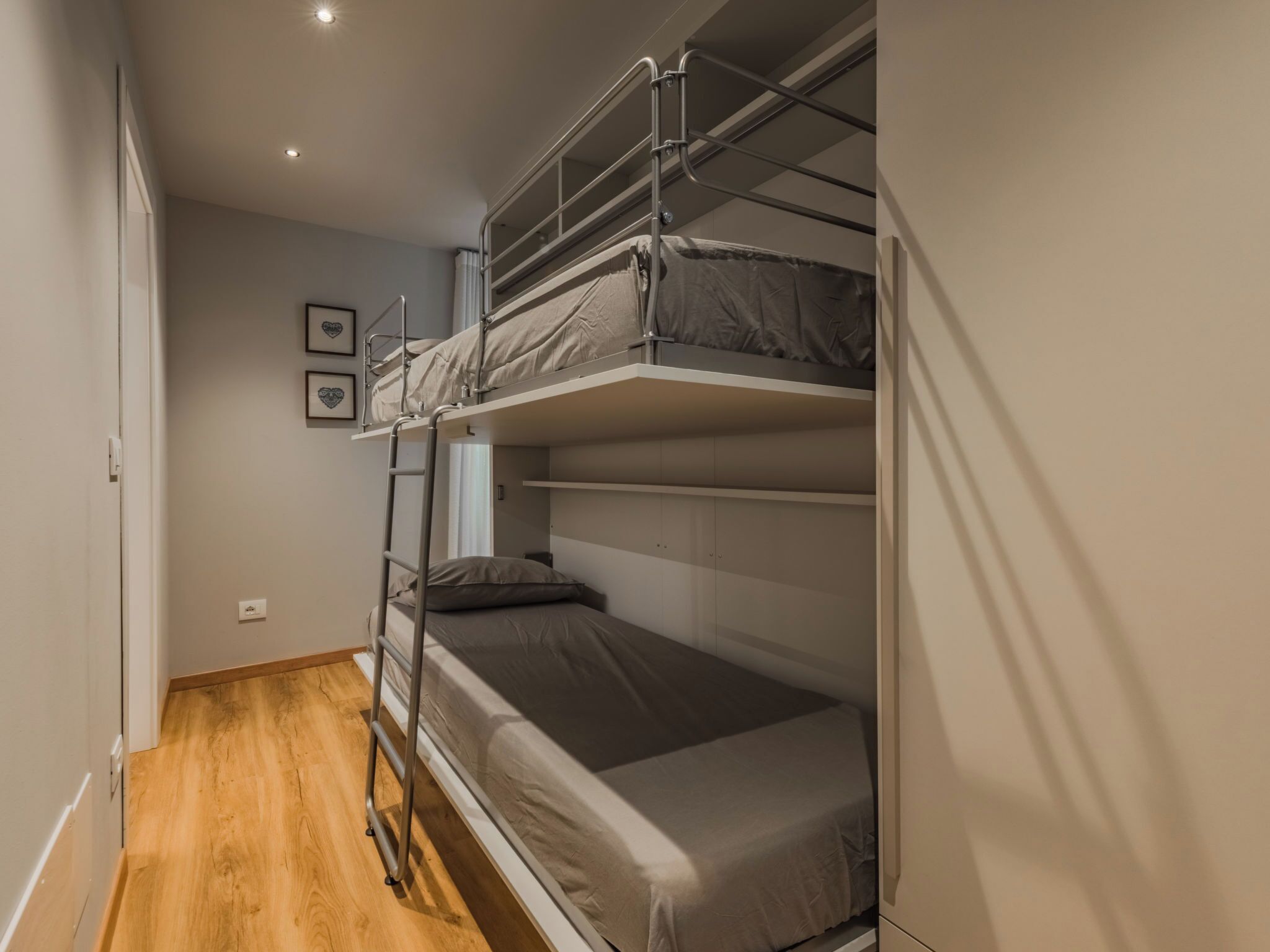 A bunk bed room with a ladder, wooden flooring, and a white wall with a picture.