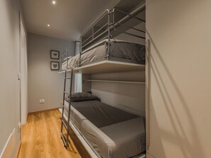 Een slaapkamer met een stapelbed, houten vloer en een witte muur met een afbeelding.