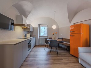 A compact kitchen with a built-in oven, a dining area with a round table and chairs, and a bright orange refrigerator. - La Fiamma by Interhome (Pellizzano)