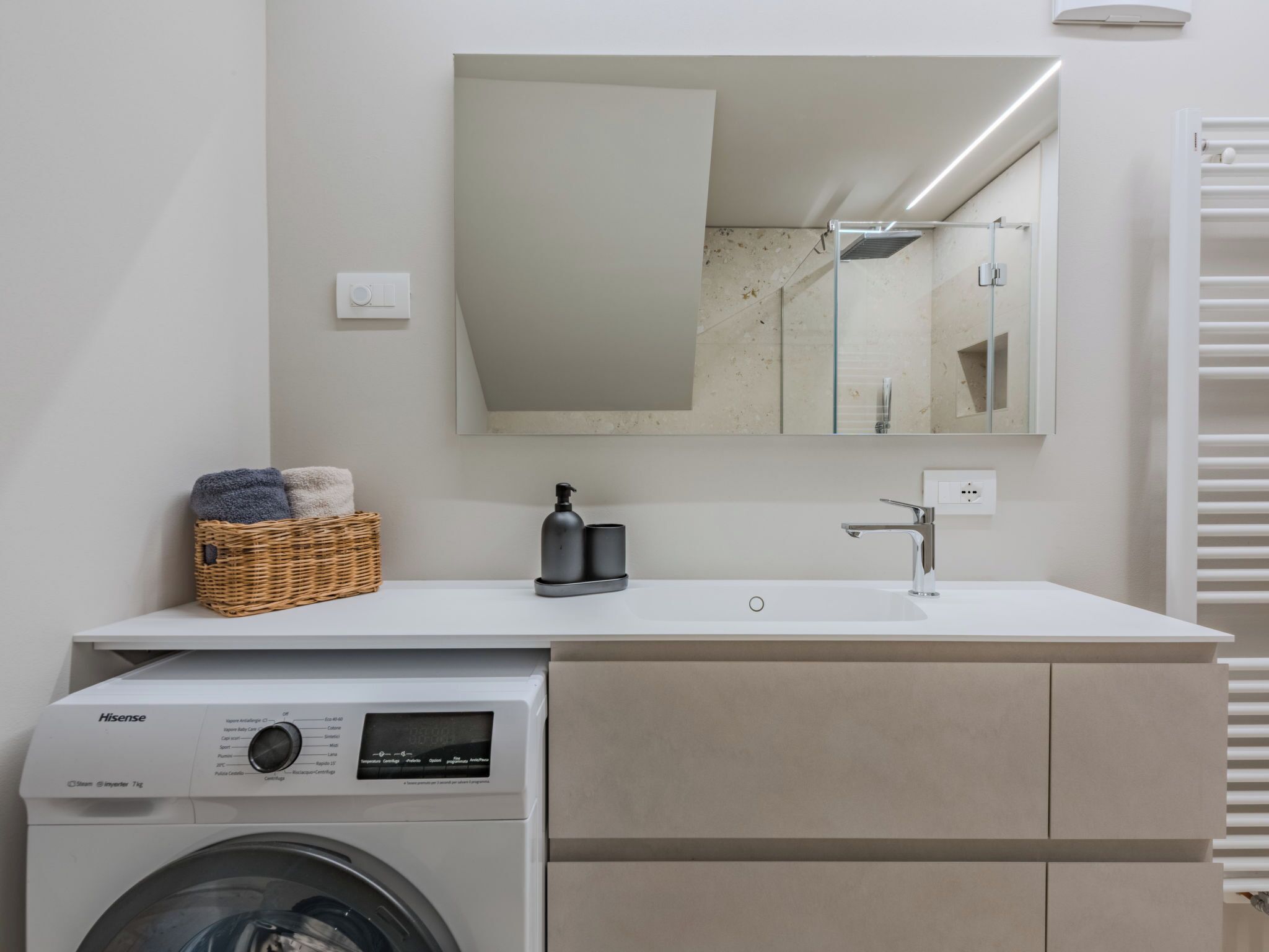 Ein modernes Badezimmer mit Waschmaschine, Waschbecken, Spiegel und Wäschekorb.