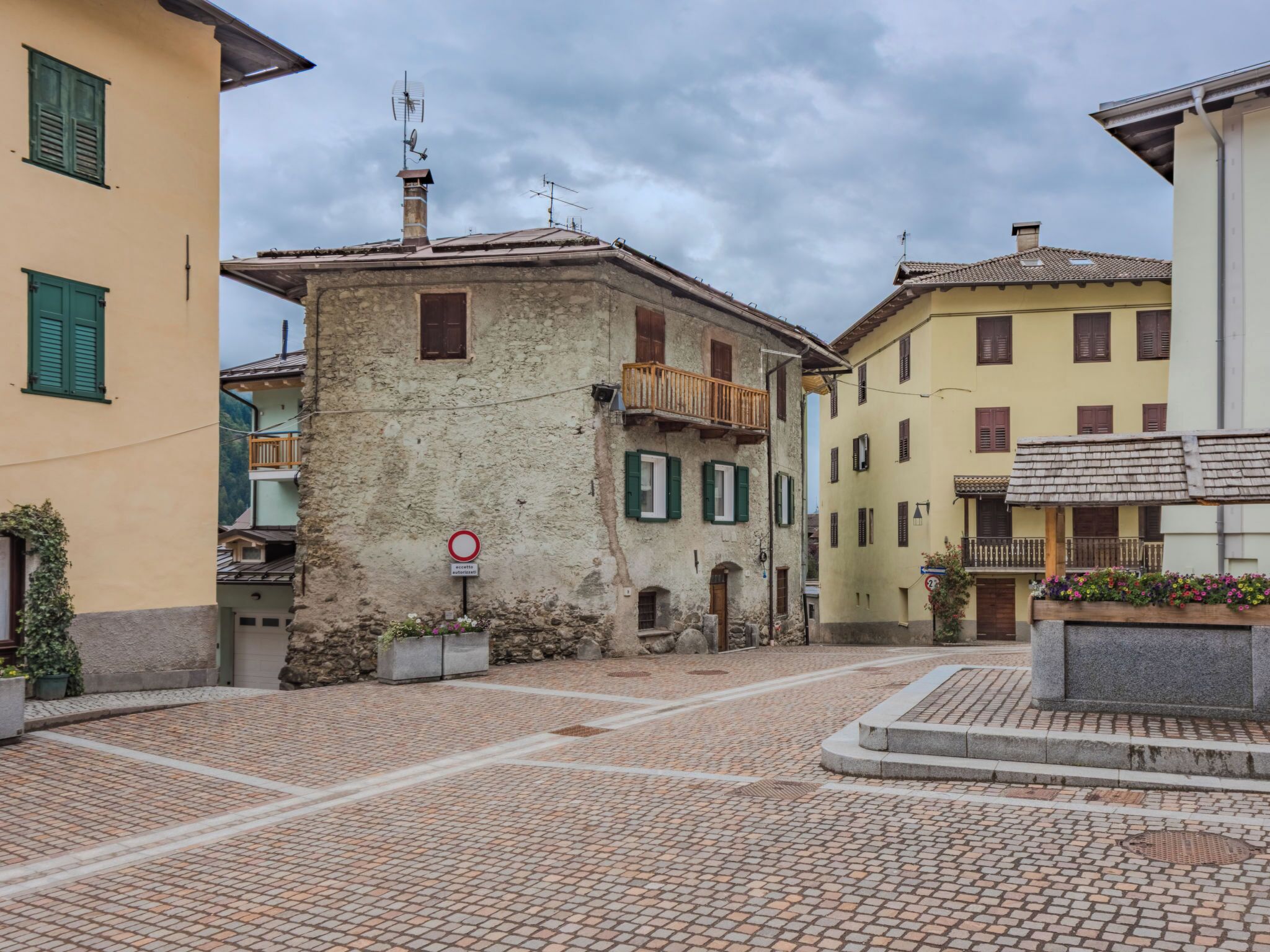 Une rue pavée bordée de bâtiments historiques, un panneau indiquant qu’il est interdit de se garer et une fontaine en pierre.