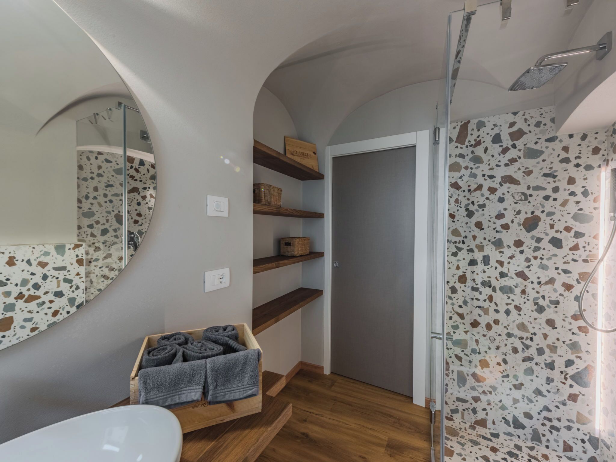 Een badkamer met een spiegel, planken, een douche en een houten bankje met handdoeken.