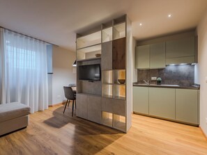 A modern living room with a TV, a dining area, and a kitchen with green cabinets. - La Spada by Interhome (Pellizzano)