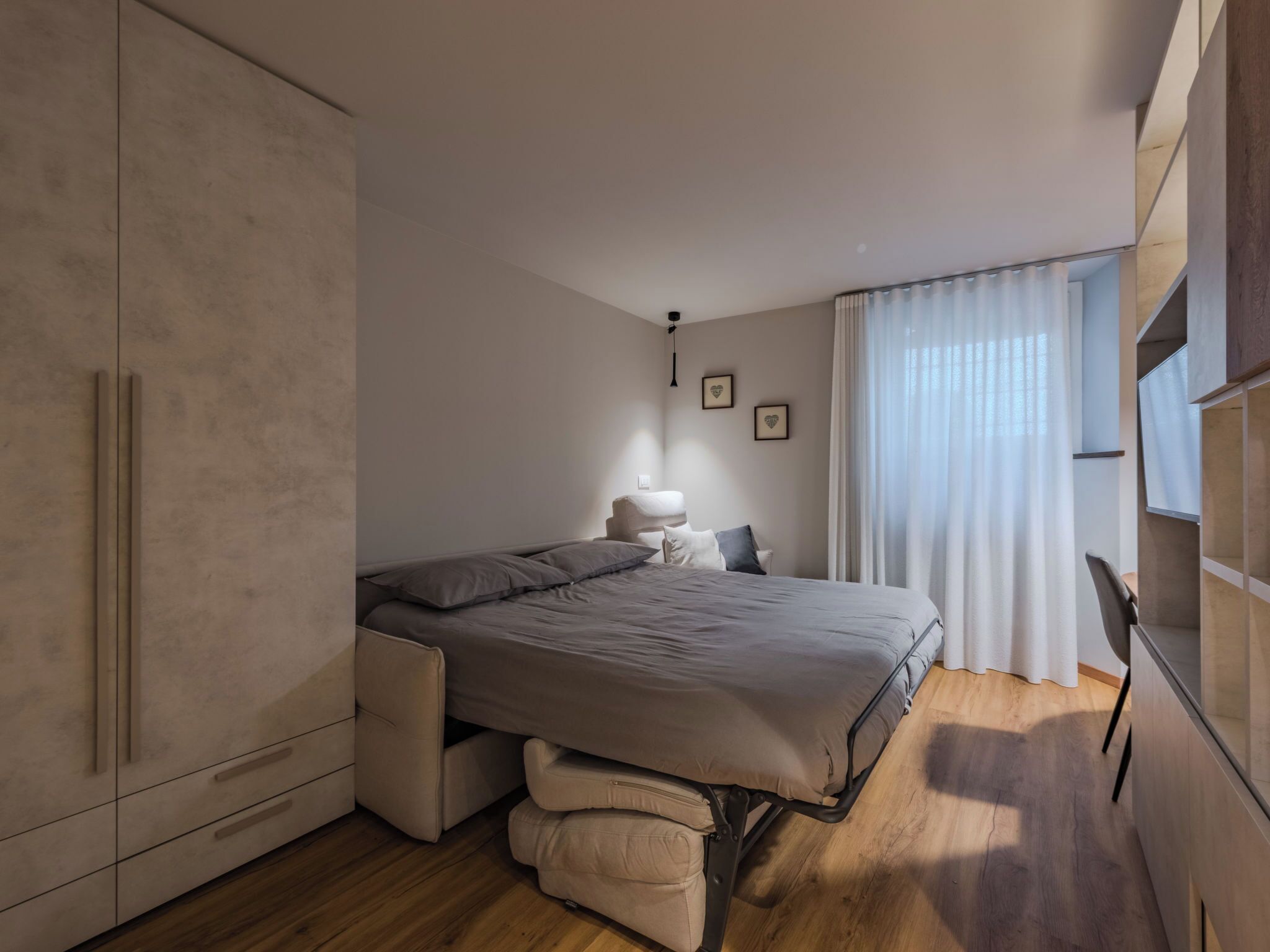 A bedroom with a bed, a wardrobe, a bedside table, and a window with curtains.