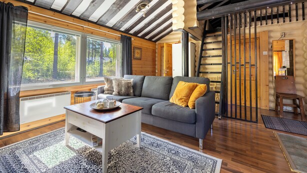 A log cabin interior with a sofa, a table, a window, and a door. - Villa Succa (Kittilä)