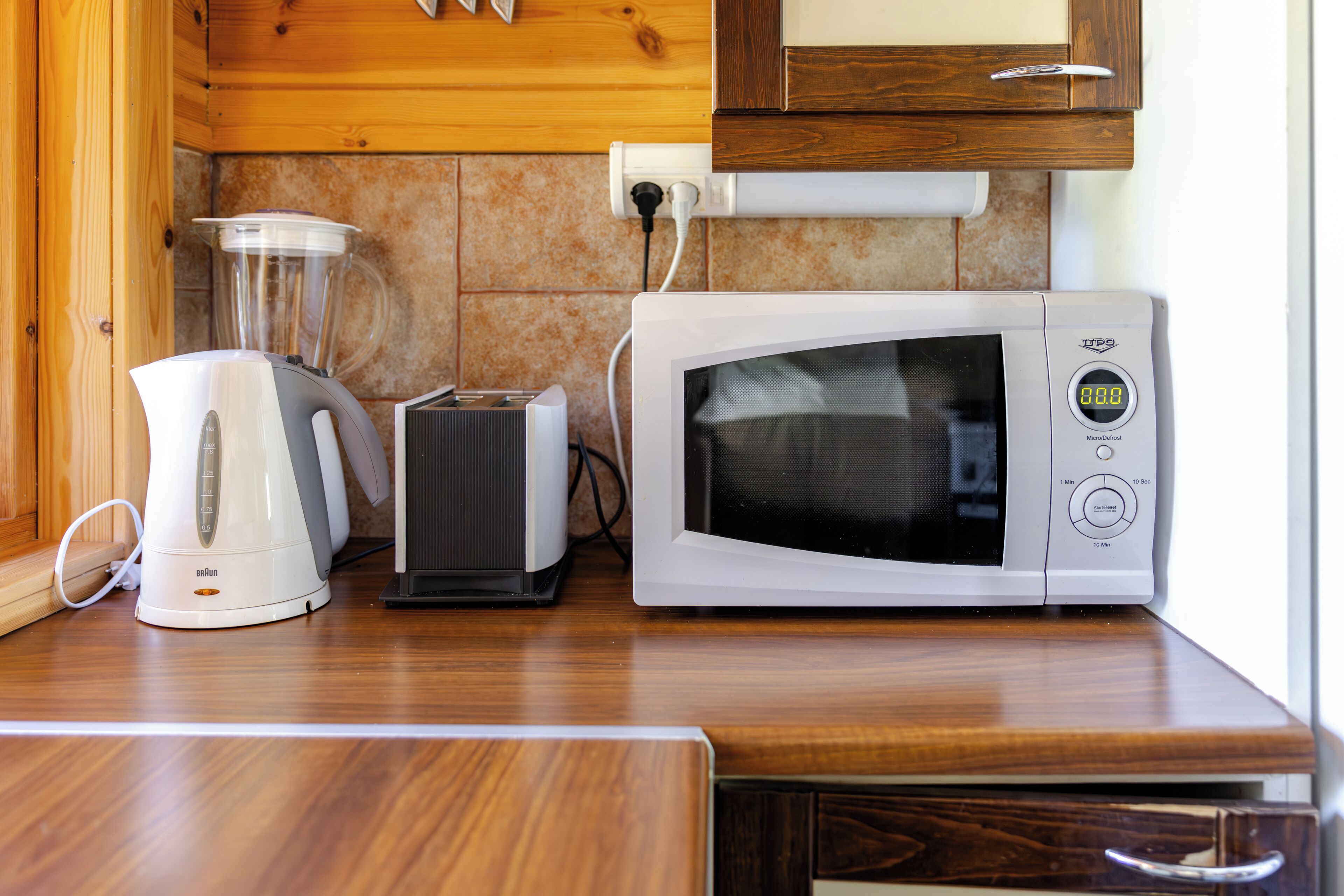 A kitchen with a microwave, toaster, and blender on a wooden countertop.