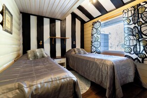 A room with two beds, a wooden ceiling, a window with patterned curtains, and a small shelf. - Villa Succa (Kittilä)