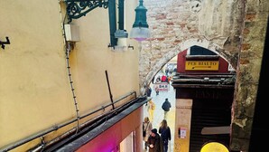 Un vicolo stretto con un negozio ben illuminato a sinistra, un cartello per 'Pasticceria Bar Rizzardi' al centro e un oggetto giallo circolare a destra.