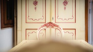 Un letto con una testiera bianca e una porta con decorazioni rosse a motivi floreali.