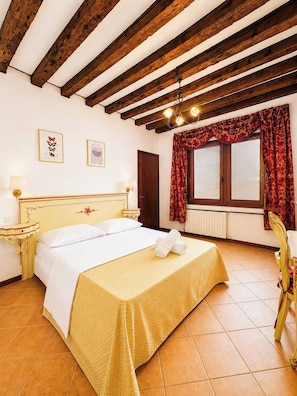 Camera d'albergo con un letto, un comodino, una lampada, una finestra con tende e un soffitto in legno.