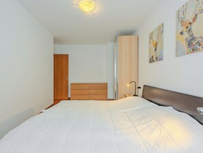Um quarto com cama, guarda-roupa, mesa de cabeceira e criado-mudo.
