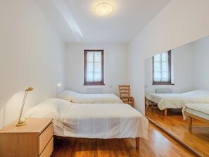 Een slaapkamer met twee bedden, een houten dressoir, een stoel en een grote spiegel die de kamer weerspiegelt.