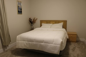 A neatly made bed with a wooden headboard, a bedside table, and a vase with dried flowers. - Lovely guest Suite in Calgary (Calgary)