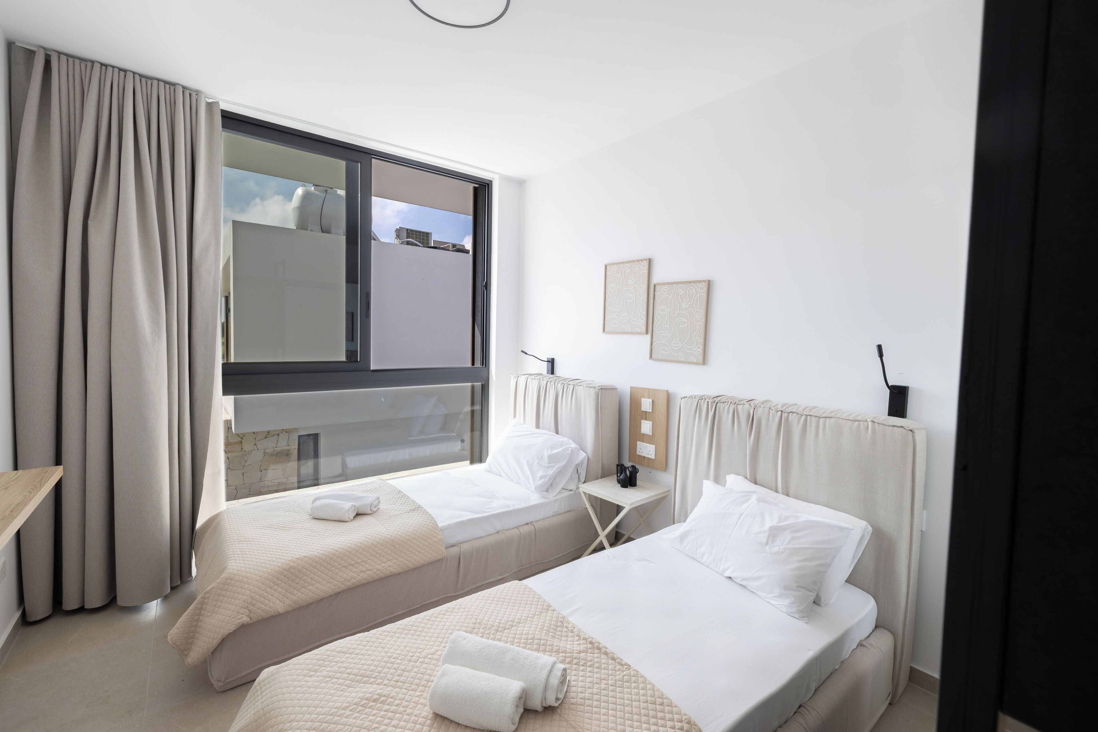 Ein Hotelzimmer mit zwei Betten, einem Fenster, einem Nachttisch und einem an der Wand befestigten Telefon.