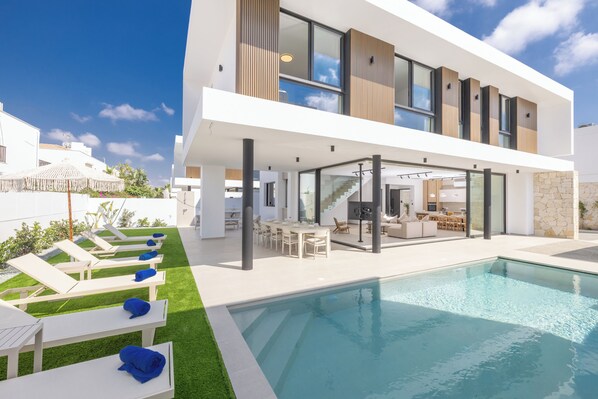 A modern two-story house with a swimming pool, outdoor seating, and a kitchen area. - New 4 bedroom villa with pool, 100 Meters from the beach (Paralimni)