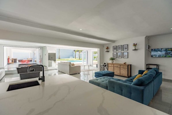 A spacious living area with a large white coffee table, a blue sofa, and a dining area with red chairs.