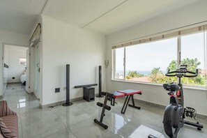 Ein Fitnessraum mit Trainingsgeräten, einem Fenster mit Blick und einer Tür zu einem weiteren Raum.