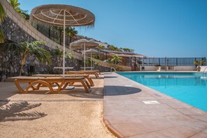 Ein Poolbereich mit Liegestühlen, Sonnenschirmen und freiem Blick auf den Pool.