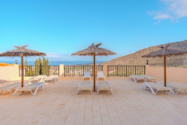 Eine Dachterrasse mit weißen Liegestühlen und Strohdächern, mit Blick auf eine Küstenlandschaft.