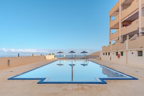 Ein Swimmingpool mit freiem Blick auf das Meer, ein Gebäude mit Balkonen und eine geflieste Terrasse.