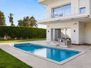 Ein modernes, zweistöckiges Haus mit Swimmingpool, überdachter Terrasse und Blick ins umliegende Grün.