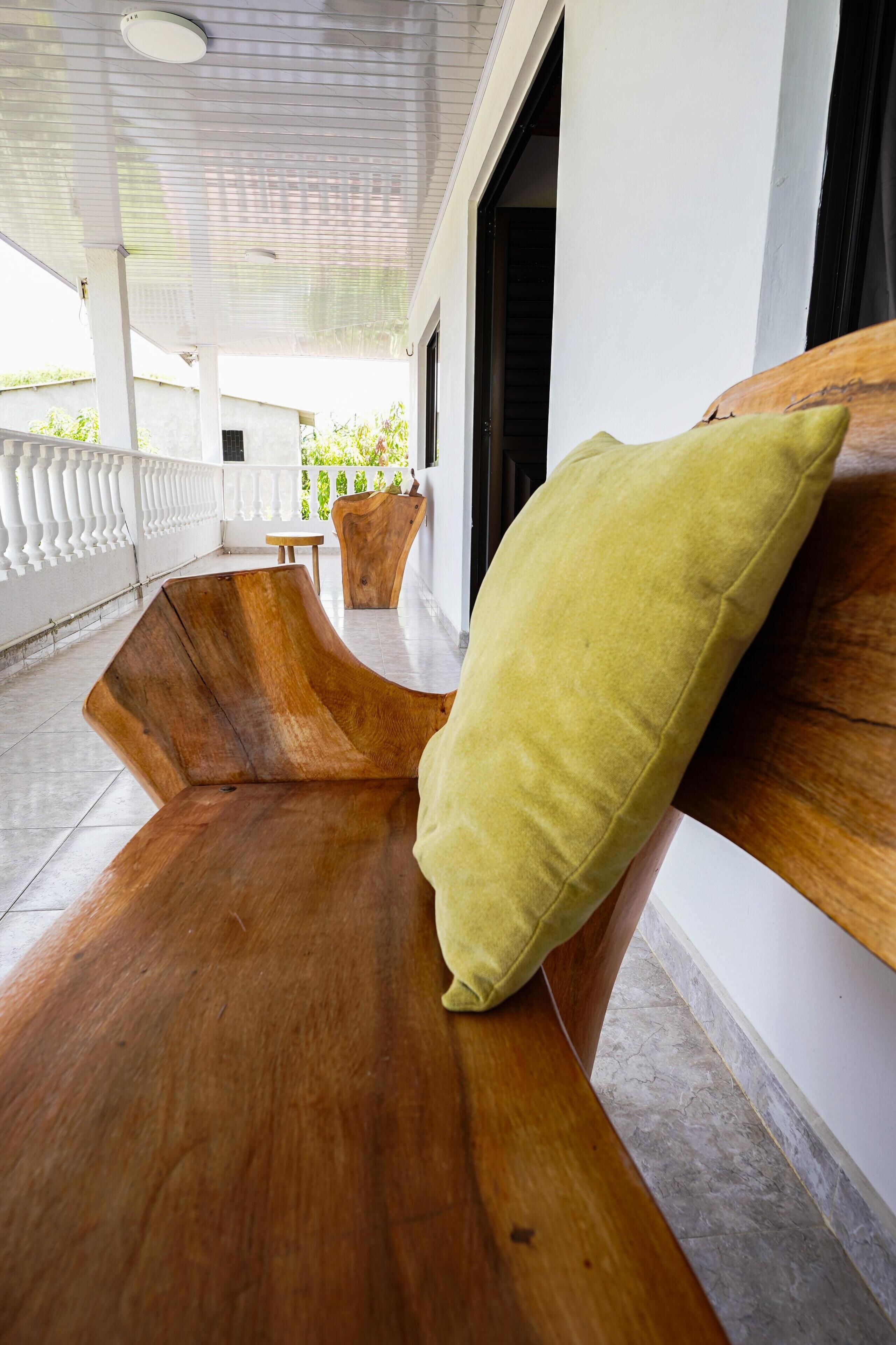 A wooden bench with a cushion, a small table, and a view of greenery through a window.