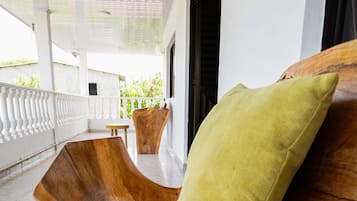 A wooden bench with a cushion, a small table, and a view of greenery through a window.
