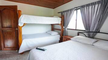 A room with bunk beds, a wooden door, a window with curtains, and a bedside table.