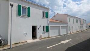 Eine Straße mit weißen Gebäuden, grünen Fensterläden und einem Fahrrad, das am Gehweg abgestellt ist.